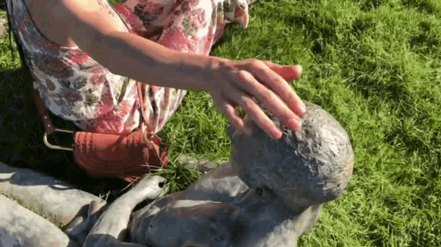 a woman in a floral dress touches a statue in the grass