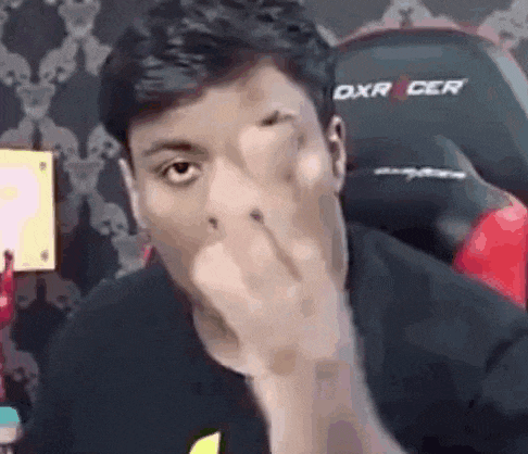 a man is covering his face with his hand and looking at the camera .