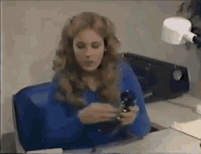 a woman in a blue shirt is sitting at a desk holding a bottle of pills .
