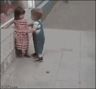 a little boy and a little girl are fighting on the sidewalk .