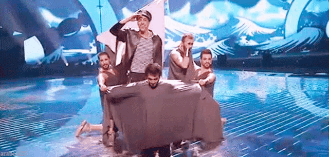 a group of men are performing on a stage and one of them is holding a blanket