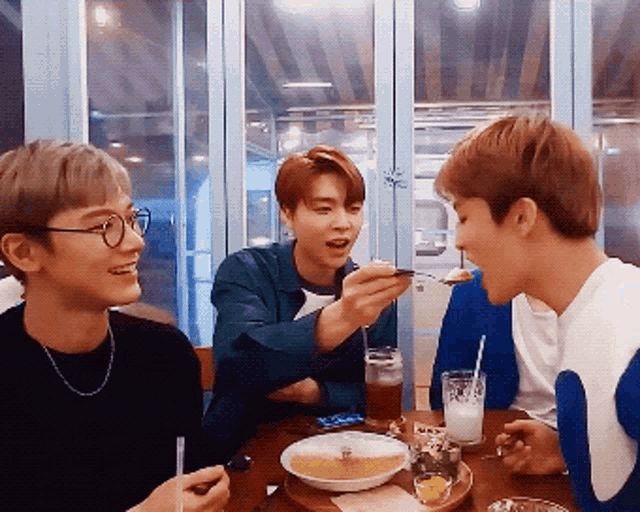 a group of young men are sitting at a table eating and drinking