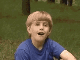 a young boy in a blue shirt is sitting in the grass .