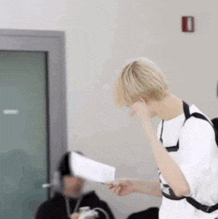 a young man with blonde hair is holding a piece of paper in a room .