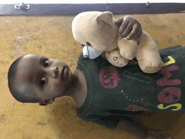 a young boy holding a teddy bear wearing a green shirt that says " i love you "