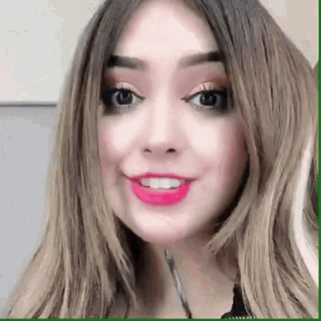 a close up of a woman 's face with long hair and red lipstick smiling .
