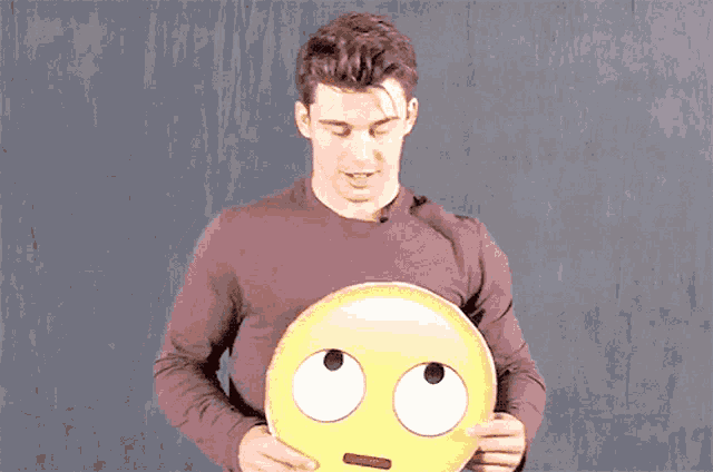 a man in a brown shirt is holding a smiley face with big eyes