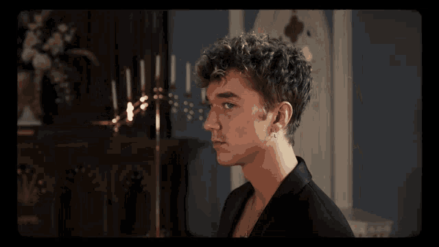 a young man with curly hair looks at the camera in front of a candle holder