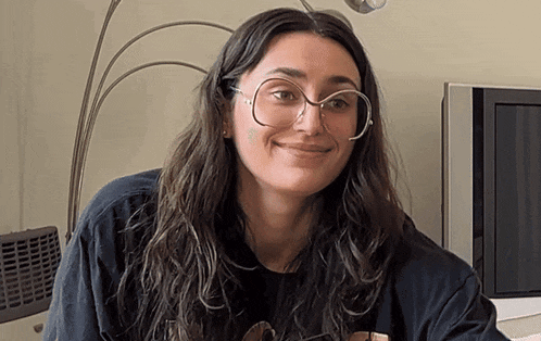 a woman wearing glasses is smiling in front of a tv