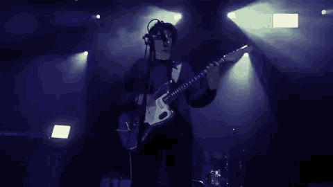 a man is playing a guitar and singing into a microphone on a stage