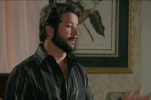 a man with a beard in front of a framed picture of a flower