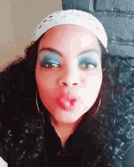 a woman wearing blue eye shadow and red lipstick blowing a kiss