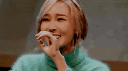 a woman in a green sweater is covering her mouth with her hand .