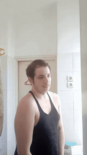 a shirtless man stands in front of a bathroom mirror