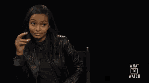 a woman in a leather jacket is sitting in a chair with what to watch written on the screen