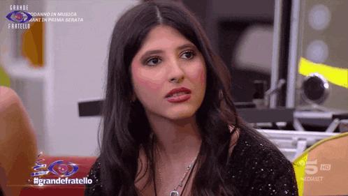 a woman is sitting in front of a sign that says grande fratello on it
