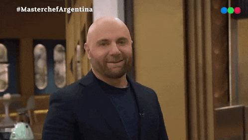 a bald man in a suit is smiling in front of a sign that says " masterchef argentina "