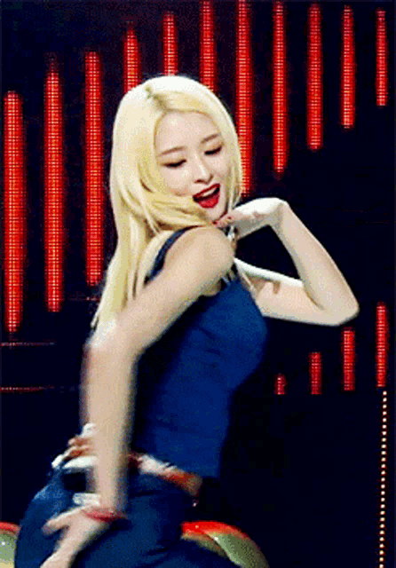 a woman with blonde hair is dancing on a stage with red lights behind her