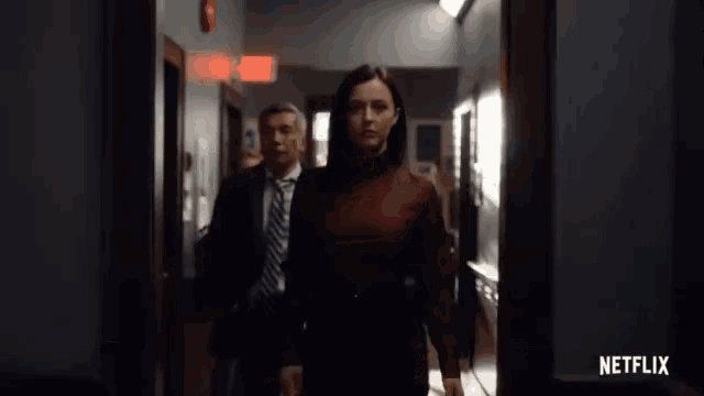 a man and a woman are walking down a hallway with netflix written on the bottom of the screen