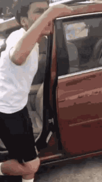 a man in a white shirt and black shorts is kneeling down in front of a red car .