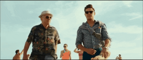a man wearing sunglasses stands next to another man wearing a hat