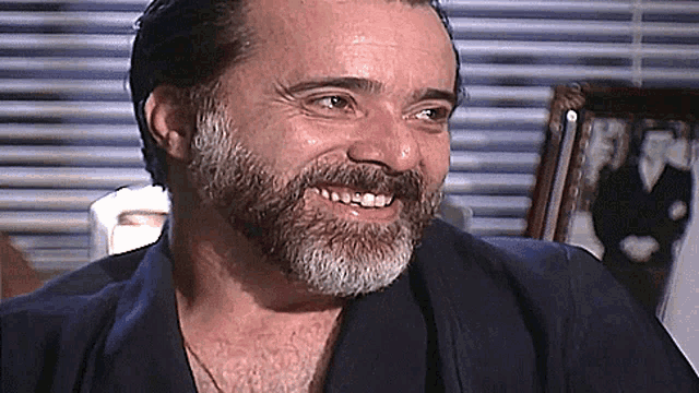 a man with a beard is smiling in front of a window