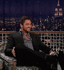 a man in a suit sits in a chair with his feet up in front of a city skyline