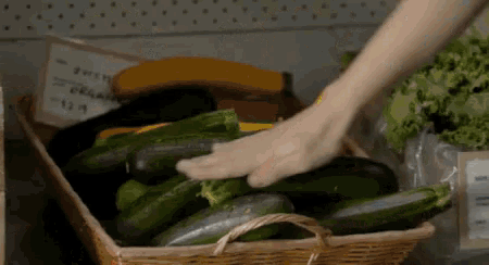 a person is touching a basket of zucchini in a grocery store .