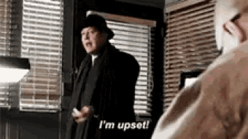 a man in a hat is standing in front of a window and saying `` i 'm upset ! ''