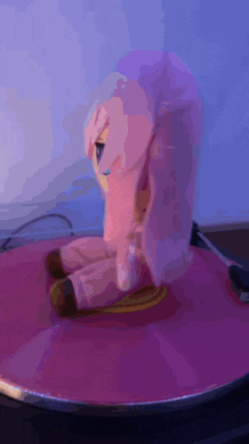 a pink stuffed animal with purple hair is sitting on a pink surface