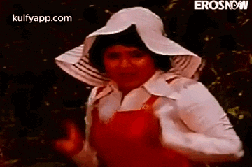 a woman wearing a white hat and red overalls is dancing in a forest .