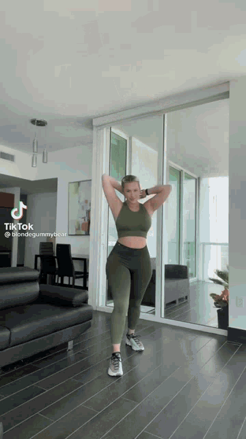 a woman in a green crop top and leggings is dancing in a living room .