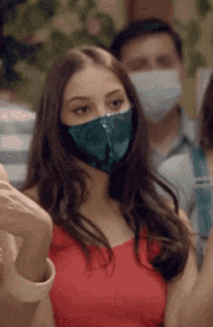 a woman wearing a mask and a red top is standing in a crowd .