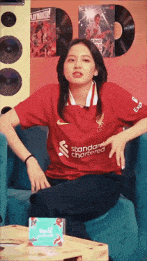 a woman is sitting on a couch wearing a red shirt that says standard chartered .