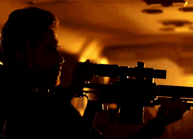 a silhouette of a man holding a rifle in a dark room