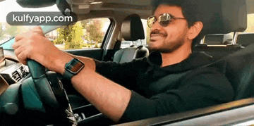 a man is driving a car wearing sunglasses and a watch .