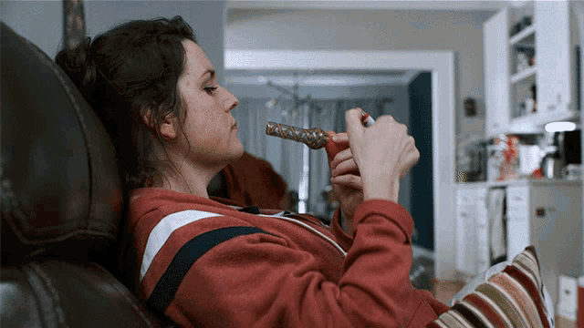 a woman in a red sweatshirt is laying on a couch smoking a pipe