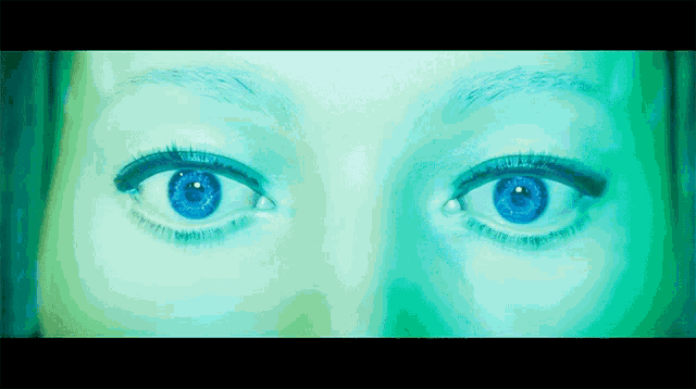 a close up of a woman 's blue eyes in a green background