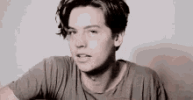a young man with long hair is wearing a t-shirt and looking at the camera .