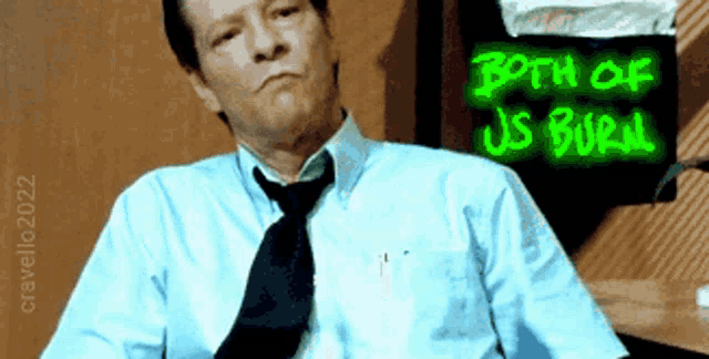 a man in a blue shirt and tie is sitting in front of a sign that says both of us buried