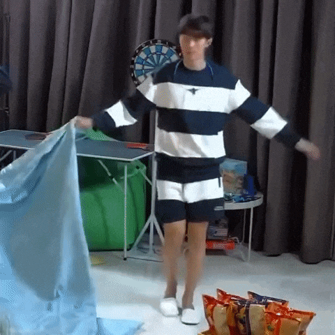a man in a striped shirt and shorts is dancing in a room with a dart board in the background .