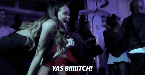 a woman in a red dress is dancing in a dark room and says yas biiiiiitch