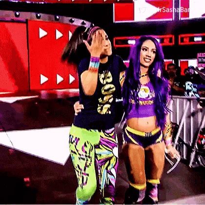 two women are standing next to each other on a stage . one of the women is wearing a purple shirt .