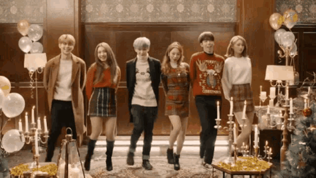 a group of people are standing in a room with candles and balloons and one has a christmas sweater on