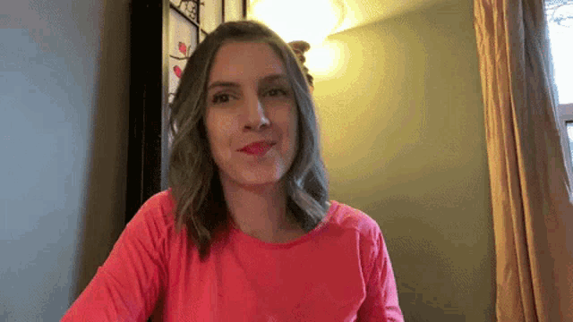 a woman wearing a red shirt is sitting in front of a window