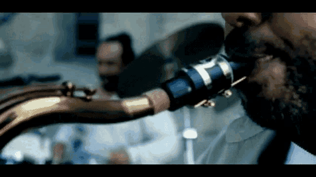 a man with a beard is playing a saxophone with the letter t on the mouthpiece