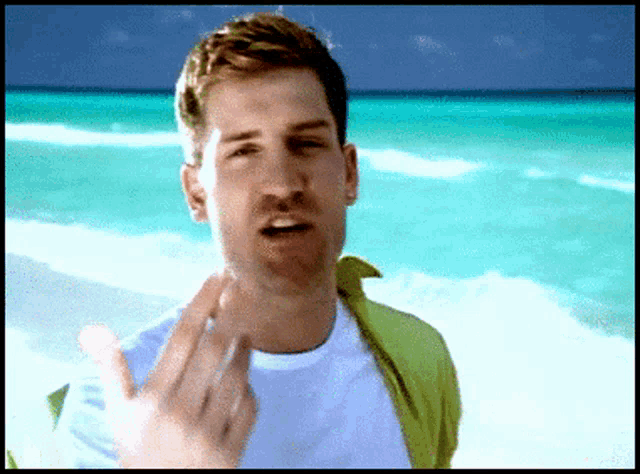 a man in a white shirt and green jacket is standing on the beach