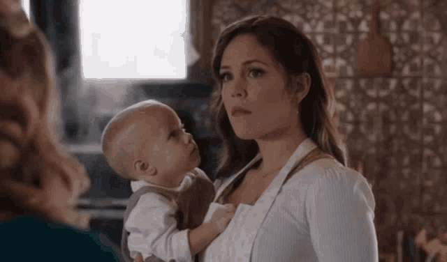 a woman is holding a baby in her arms and looking at the camera