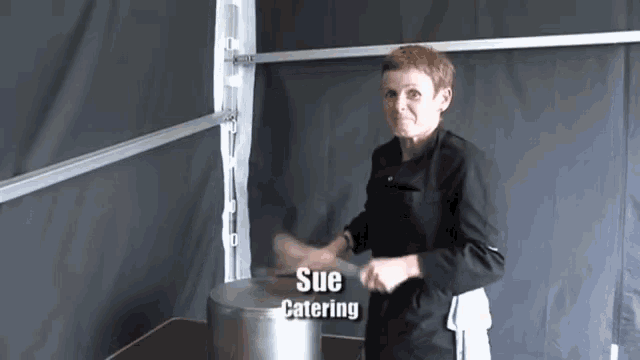 a woman is standing in front of a large pot with the name sue catering written on it