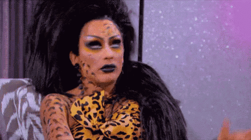 a drag queen is sitting on a couch wearing a leopard print outfit and makeup .